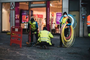 ouvriers en gilets jaunes installant des câbles optiques dans une rue commerçante, transition réseau cuivre