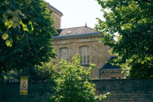 A charming stone building hidden among vibrant trees with a school sign nearby, captured on a sunny day.