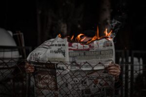 Person holding a burning newspaper outdoors, representing chaos or protest.