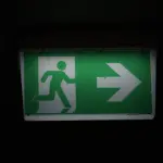 Illuminated green emergency exit sign with an arrow pointing right in a dark setting.