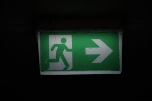 Illuminated green emergency exit sign with an arrow pointing right in a dark setting.